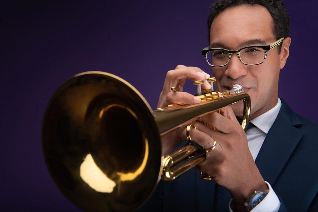 James Suggs playing the trumpet in front of purple background.